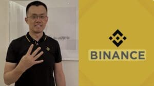 Čovjek s očalama pozira s Binance logom u pozadini, odjeven u crnu polo majicu.