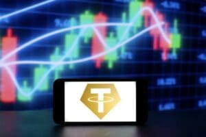 Pametni telefon s Tether logom ispred grafikona tržišta kriptovaluta.