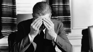 Muškarac u odijelu sjedi za stolom, prekriva lice rukama, stres u uredu.