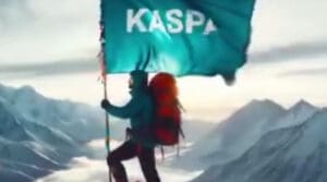 Penjač na vrhu planine s zastavom KASPA i snježnim pejzažom.